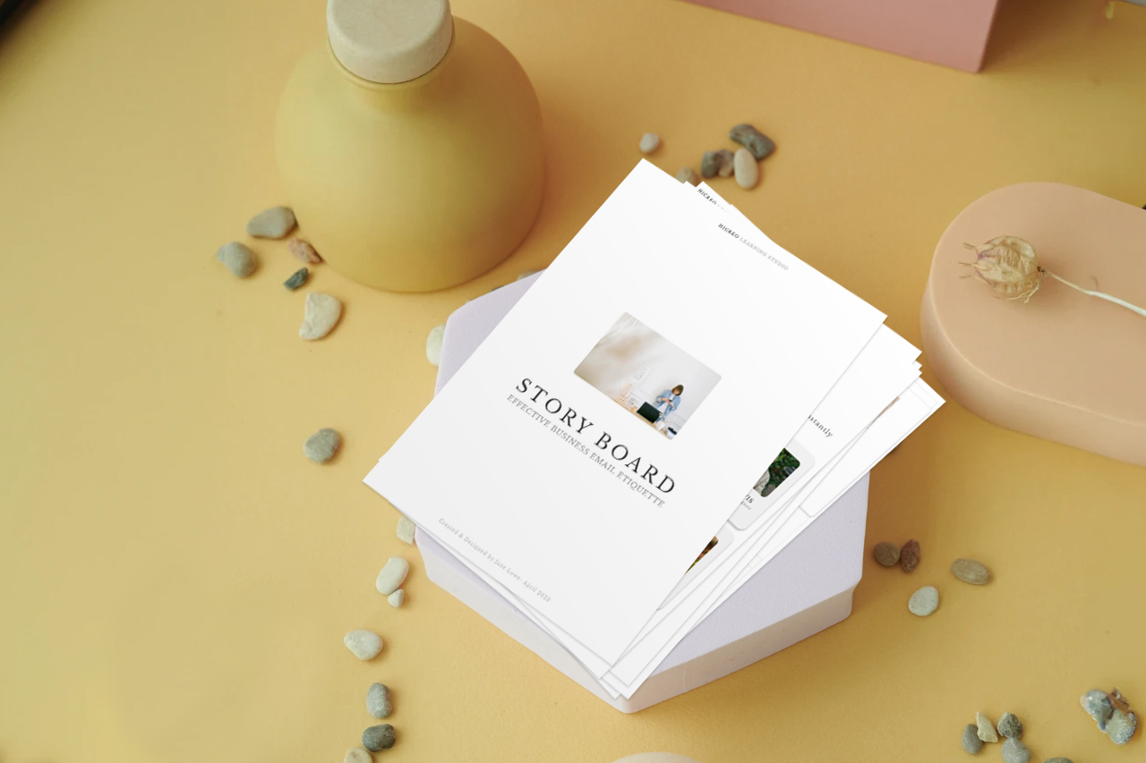 An eLearning storyboard on a mustard-colored desk, surrounded by pebbles, a bottle, and dried flowers.