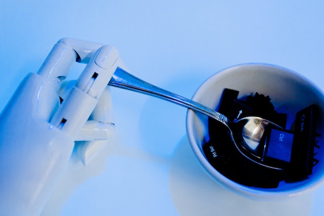 A robot hand holds a spoon over a bowl of keyboard keys, with a sky blue background. The hiCreo elearning platform uses AI and text generation to design innovative learning experiences