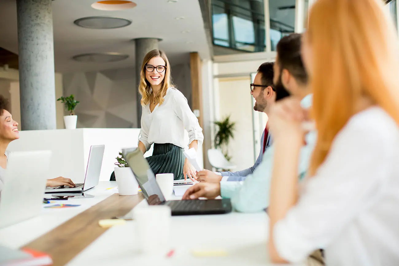 Smiling woman presenting to colleagues in a modern office, showcasing how to create presentations with AI using an AI presentation maker and professional presentation templates.